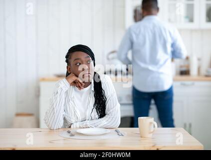 Portrait Of Thoughtful Young Black Woman Sitting At Table In Kitchen Stock Photo