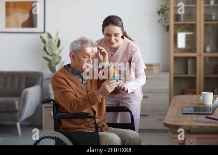 Portrait of senior man in wheelchair using smartphone with caregiver helping him at retirement home, copy space Stock Photo
