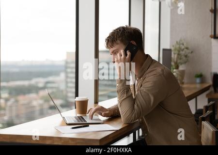 Close up confident businessman talking on phone, using laptop Stock Photo