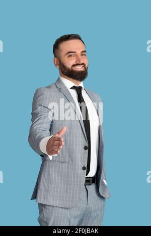 Successful millennial businessman offering his hand for handshake over blue studio background Stock Photo