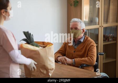 Portrait of smiling senior man in wheelchair talking to woman holding grocery bag, assistance and food delivery service, copy space Stock Photo