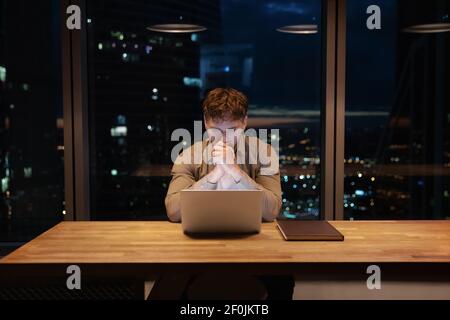 Thoughtful businessman working on laptop at night, developing project strategy Stock Photo