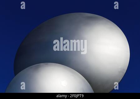 Closeup of two abstract isolated metallic silver colored shiny round sphere discs against dark deeep blue sky Stock Photo