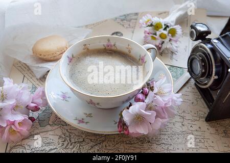 Black coffee in a cup, next to a world map and an old camera with spring flowers on the table Stock Photo