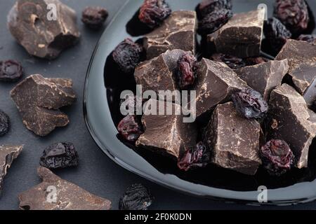 Pieces of homemade broken dark chocolate and raisins on a black plate. Low key. Close up. Stock Photo