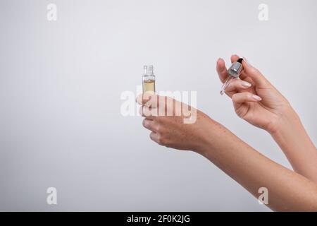 Cropped view of mature woman applying regenerating anti-aging serum onto her hands over light background, copy space Stock Photo