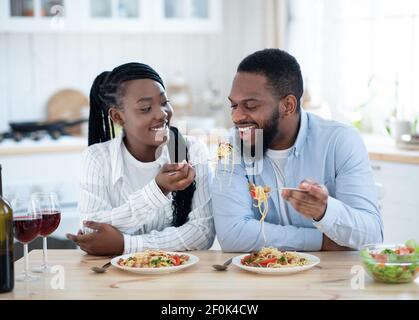 Joyful Black Spouses Having Lunch At Home, Eating Spaghetti And Drinking Wine. Stock Photo
