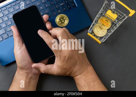 male hands using smartphone for sell or buy  virtual money, bit coin in yellow trolley and laptop on black background, electronic virtual money for we Stock Photo