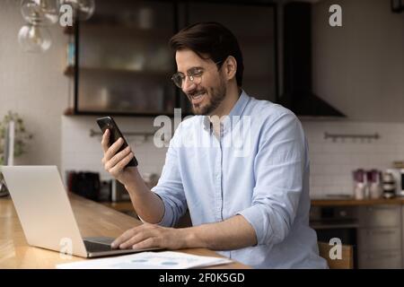 Close up smiling businessman wearing glasses using laptop and phone Stock Photo