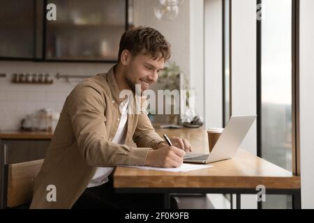 Close up smiling man using laptop, taking notes, studying online Stock Photo