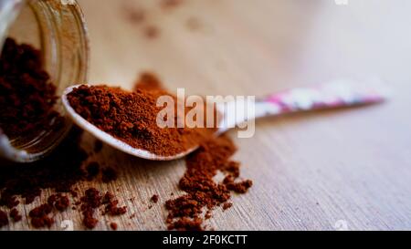 Coffee powder spilling on the wooden table ground with white spoon. Pile of brown coffee with a jar in blur background. Macro top view, India Stock Photo