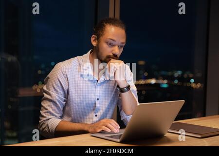 Close up thoughtful African American businessman using laptop at night Stock Photo