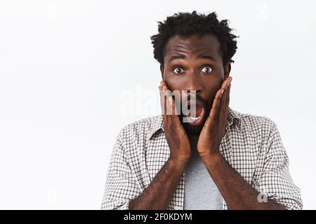 Surprised, speechless handsome african-american guy, gasping and scream from fear or amazement, open mouth, drop jaw and touch face astonished, stare Stock Photo