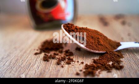 Coffee powder spilling on the wooden table ground with white spoon. Pile of brown coffee with a jar in blur background. Macro top view, India Stock Photo