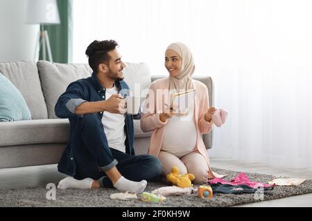 Happy pregnant muslim couple getting geady for childbirth, making checklist at home Stock Photo