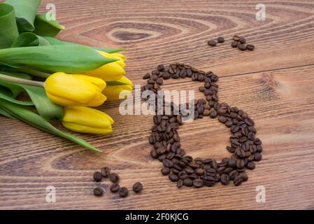 Yellow tulips on a dark wooden background with coffee beans in the form of March 8. Greeting card for women's day Stock Photo