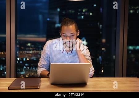 Close up thoughtful African American businessman using laptop at night Stock Photo