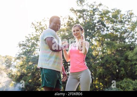 Fitness couple in park with woman giving thumbs-up to camera Stock Photo