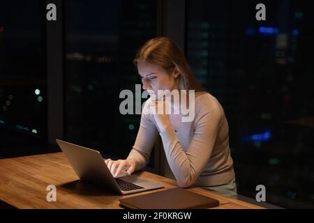 Close up thoughtful businesswoman using laptop, working at night Stock Photo