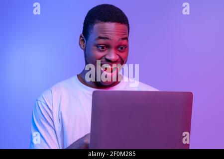 Closeup Shot Of Excited Black Guy Using Laptop Computer Under Neon Lighting Stock Photo