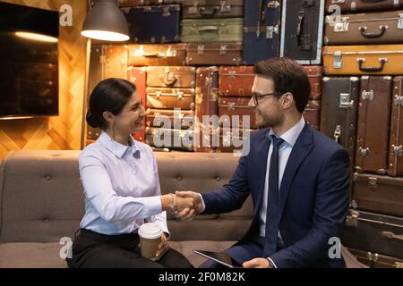 Happy diverse business people shaking hands, sitting on couch Stock Photo