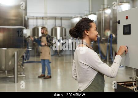 Side view portrait of young female worker operating machines in brewery workshop, copy space Stock Photo