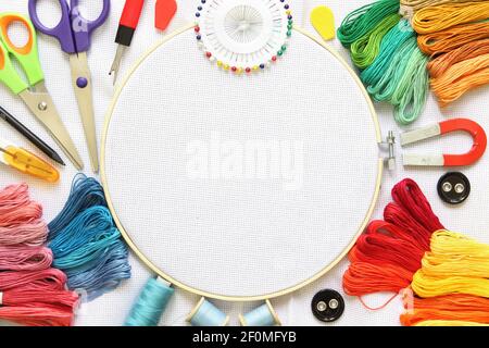 Embroidery hoop and multicolored accessories on white linen canvas with spools of thread, needle and scissors. Stock Photo