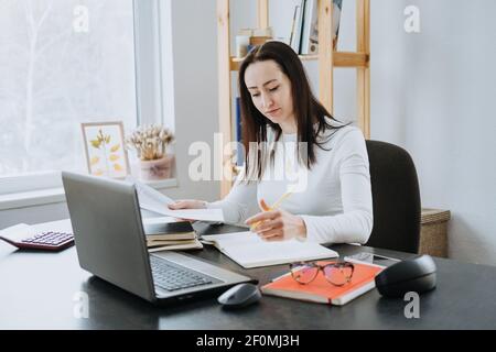 Remote Accounting Finance Jobs. Online Accounting Solution. Candid portrait of female accountant working with laptop, calculator and documents at home Stock Photo