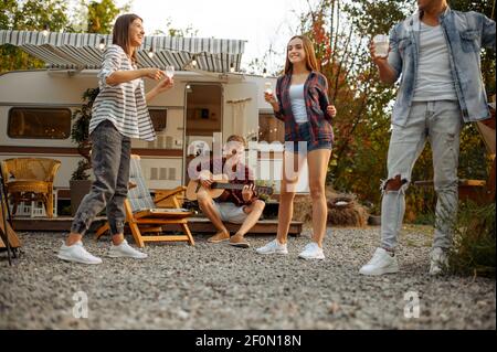 Friends playing on guitar and dancing at camping Stock Photo