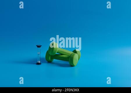 two green dumbbells and an hourglass on a blue background Stock Photo