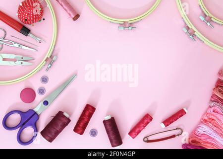 Sewing accessories on a pink background with needles, spool of thread, scissors and a tape measure