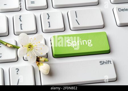 Green key with Spring word and cherry blossom on white computer keyboard. Spring season mood, holidays, sales concept. Message on keypad enter button. Stock Photo