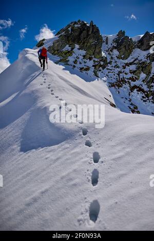 Man climbing a snowy mountain on a sunny day in Devero, Italy.