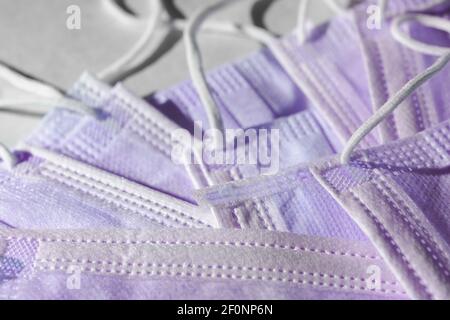 Many disposable 3-ply purple face masks in a pile. Elastic ear loop style masks often associated with surgical or medical use. Coronavirus relevance. Stock Photo