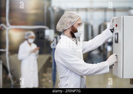 Side view portrait of male worker operating machines at chemical plant while wearing lab coat and protective clothing, copy space Stock Photo