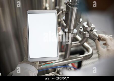 Close up of unrecognizable worker holding tablet with blank white screen while operating equipment at chemical plant, copy space mockup Stock Photo