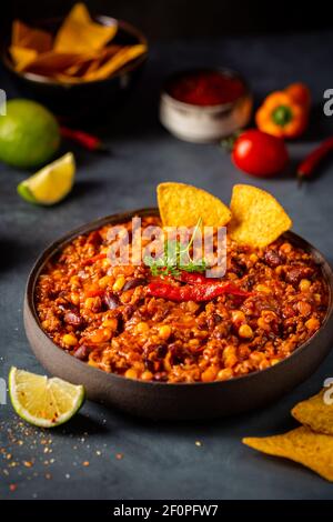 Mexican hot chili con carne in a bowl with tortilla chips on dark background Stock Photo