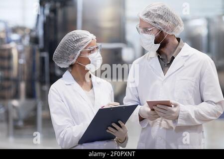 Waist up portrait of two workers wearing protective clothing while discussing production at modern chemical plant Stock Photo