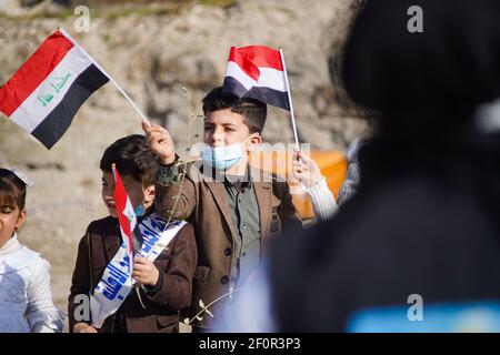 A kid waving the Iraqi flag during the papal visit. Pope Francis met the people and prayed for the souls of the war victims in Hosh al-Bieaa area near the ruins of the Al-Tahira Grand Church in the square which contains four churches all of which were damaged during the war against ISIS and this visit is considered the first papal visit in history to Iraq. Stock Photo