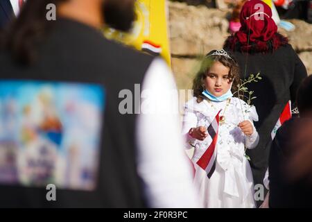 A girl holding the Iraqi flag and flowers during the papal visit. Pope Francis met the people and prayed for the souls of the war victims in Hosh al-Bieaa area near the ruins of the Al-Tahira Grand Church in the square which contains four churches all of which were damaged during the war against ISIS and this visit is considered the first papal visit in history to Iraq. Stock Photo