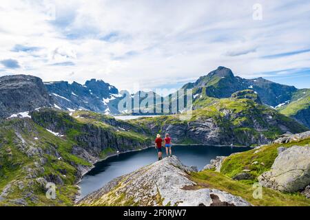 Two hikers looking over lake Tennesvatnet, mountain landscape, Moskenesoey, Lofoten, Nordland, Norway Stock Photo