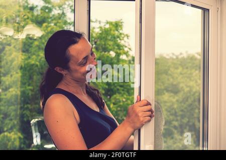 Beautiful woman cleaning window at home. A girl washes windows at home. To clean up the house. Long-haired woman cleaning windows with spray in home Stock Photo