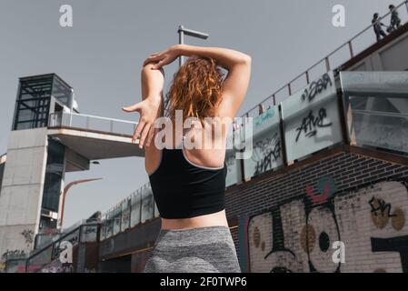 Young woman from behind, wearing a sports top and leggings, stretching her arm by bending it in the back Stock Photo