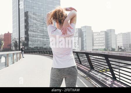 Young woman from behind dressed in sportswear on the street stretching one arm behind her head Stock Photo
