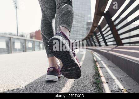 Feet of a woman dressed in sports tights walking on an asphalt ground in the street