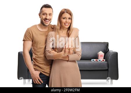 Young couple in front of a couch with a box of popcorn and ed glasses isolated on white background Stock Photo