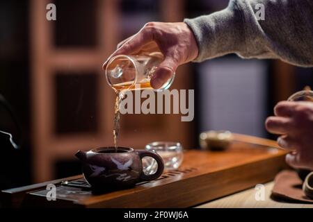 Close-up of a traditional oriental tea ritual. A man pours black ripe tea from a flask into a tasting cup. Blurry background. Stock Photo