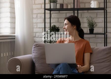 Dreamy smiling female teenager distracted from laptop screen take break Stock Photo