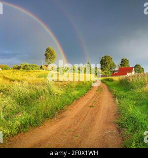 Rainbow over stormy sky. Rural landscape with rainbow over dark stormy sky in a countryside at summer evening. Stock Photo