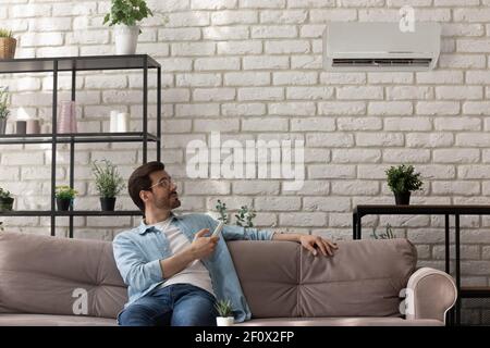 Happy young man sit on couch hold air conditioner controller Stock Photo